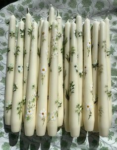 several white candles are lined up on a floral tablecloth with daisies and leaves