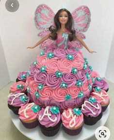 a barbie doll sitting on top of a cake with cupcakes