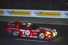 a red sports car driving on a race track at night with lights on it's side