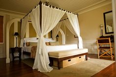 a canopy bed with white drapes in a bedroom