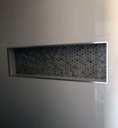 a white bathroom with hexagonal tile and stainless steel grates on the wall