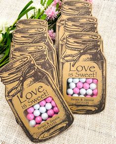 two mason jars with love is sweet candy in them sitting next to pink and white flowers