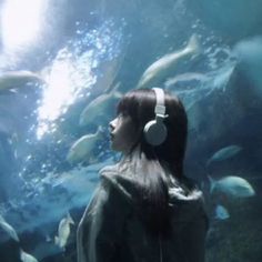 a woman wearing headphones standing in front of a large aquarium filled with lots of fish