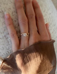 a woman's hand with a diamond ring on top of her finger, resting against a white blanket