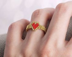 a woman's hand wearing a gold ring with red beads on it and a white background