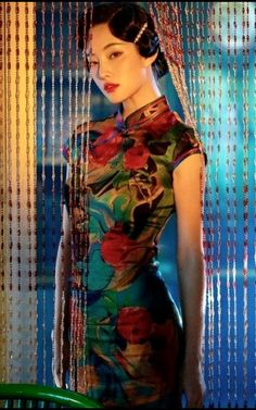 a woman standing in front of a window wearing a dress with flowers and beads on it