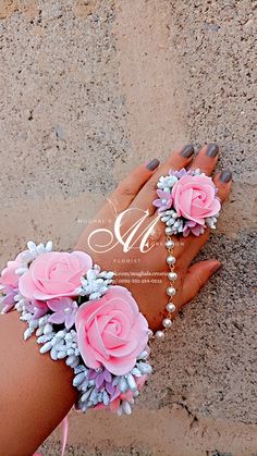 a woman's hand with pink flowers and pearls on her wrist, in the sand