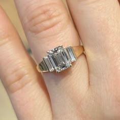 a woman's engagement ring with three baguettes on the side and an emerald cut diamond in the middle