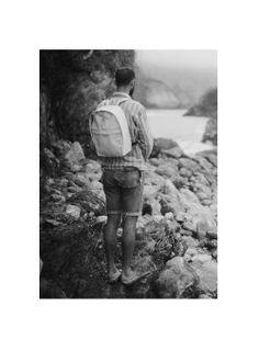 a man with a backpack standing on rocks by the ocean looking out at the water