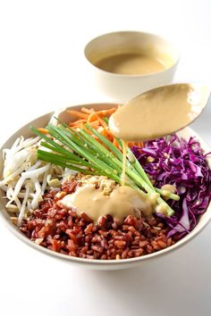 a white bowl filled with rice, meat and veggies next to dipping sauce