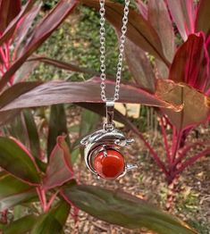 a silver necklace with a red bead hanging from it's center surrounded by leaves