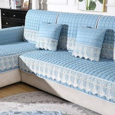 a blue couch with white lace on it in front of a dresser and window sill