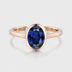 a rose gold ring with an oval blue sapphire stone in the center, on a white background