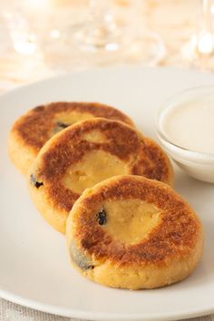 three biscuits on a plate with a bowl of cream in the background and glasses of milk to the side