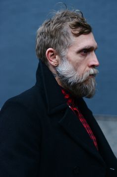 a man with a goatee and beard wearing a black coat, red checkered tie