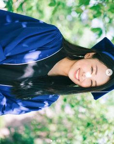 a young woman wearing a blue graduation gown and smiling at the camera with trees in the background