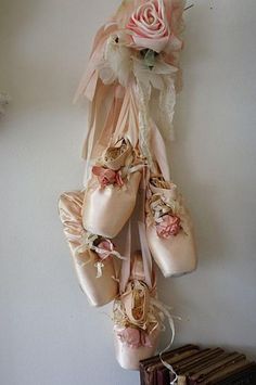 several ballet shoes hanging from a wall with flowers on them and ribbons attached to the shoelaces