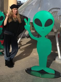 a woman standing next to a green alien statue