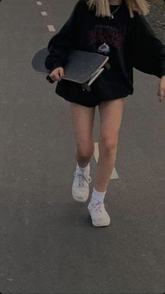 a woman walking down the street with a skateboard in her hand and wearing a black sweatshirt