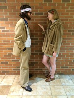 a man and woman standing next to each other in front of a brick wall wearing costumes