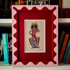 a red frame with a picture of a person in a crown on it and books behind it