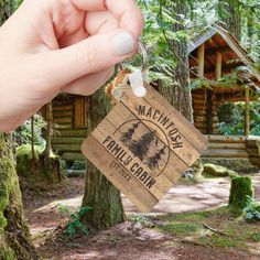 a hand holding a keychain that is in front of a tree and log cabin