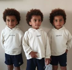 three young children standing next to each other in front of a wall wearing white sweatshirts and blue shorts