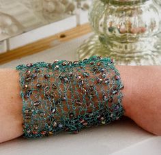 a woman's arm with a green beaded bracelet on it and a vase in the background