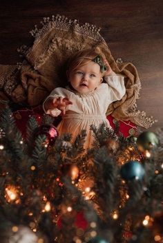 a baby laying on top of a christmas tree next to a pile of ornaments and lights