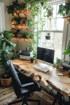 a wooden desk topped with a computer monitor next to a window filled with potted plants