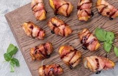 bacon wrapped around peaches on a wooden cutting board with basil leaves and sauce drizzled over them