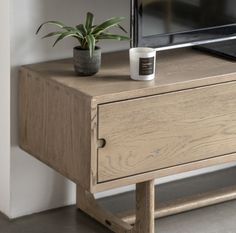 a coffee cup sitting on top of a wooden table next to a television set and potted plant