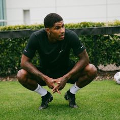 a man kneeling down on top of a lush green field next to a soccer ball