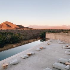 an outdoor pool with lounge chairs and mountains in the background at sunset or sunrise time