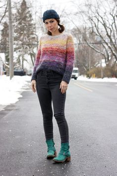 a woman standing on the side of a road wearing black jeans and a colorful sweater