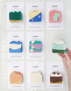 a person holding a piece of cake in front of a white tile wall with different colored cakes on it