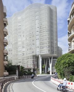 a man riding a motorcycle down a curvy road next to a tall building