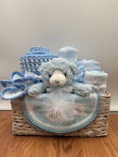 a blue teddy bear sitting in a basket filled with crocheted hats and diapers