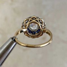 a gold ring with blue and white stones on it is being held by a metal tool