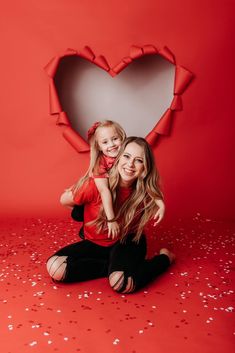 a mother and daughter pose in front of a heart shaped backdrop