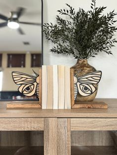 a wooden table topped with two books and a vase filled with green plants on top of it