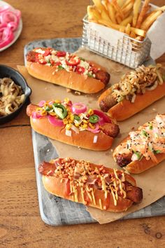 four hot dogs on buns with toppings and french fries