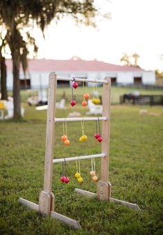 a wooden ladder with colorful balls hanging from it's sides on the grass in front of a barn