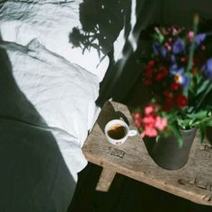 a cup of coffee sitting on top of a wooden table next to a vase filled with flowers