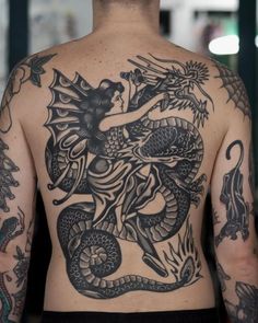 the back of a man with tattoos on his body and arms, holding a snake