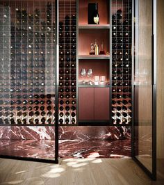 a wine cellar with glass doors and shelves filled with bottles on the wall, along with wooden flooring