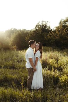 a man and woman standing in the middle of a field with trees in the background