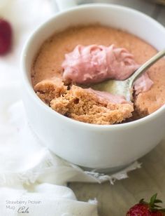 a bowl filled with pudding next to a strawberry on top of a white cloth and a spoon