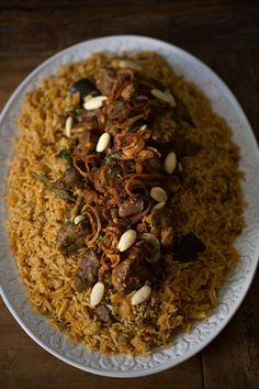 a white plate topped with rice and meat covered in sauce on top of a wooden table