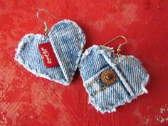 two denim heart shaped earrings on top of a red cloth covered surface with the word love written in it